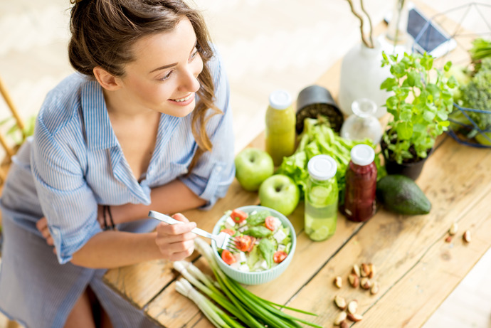 Mujer con tenedor en la mano sentada delante de un plato de ensalada