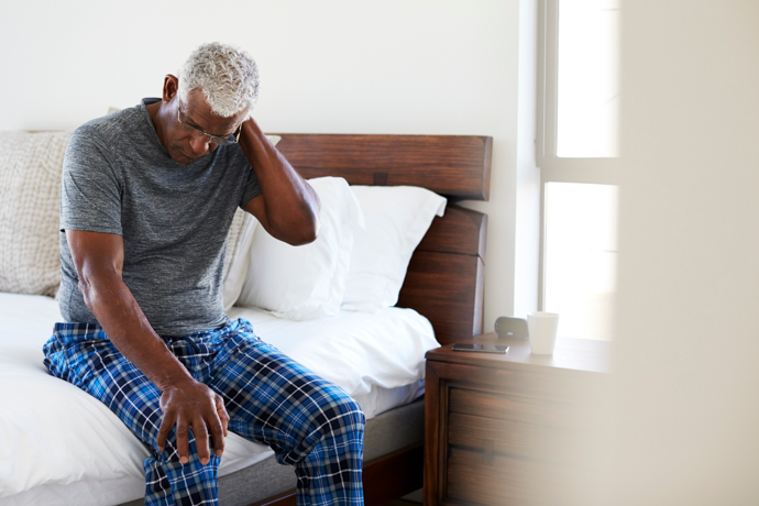 hombre canoso sentado al borde de la cama con gesto cansado