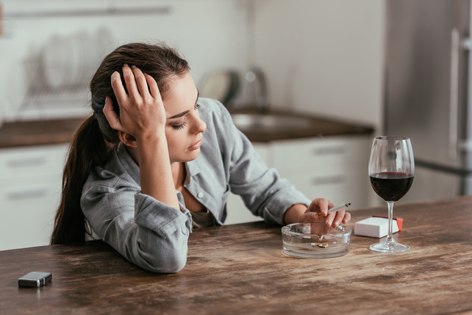 Mujer estresada mientras fuma cigarrillo y bebe vino 