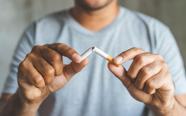 Hombre partiendo un cigarrillo al conocer los beneficios de dejar de fumar.